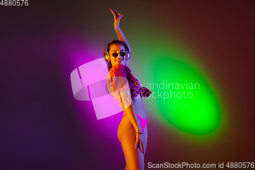 Image of Beautiful seductive girl in fashionable swimsuit on disco bicolored neon studio background in neon light. Summer, resort, fashion and weekend concept
