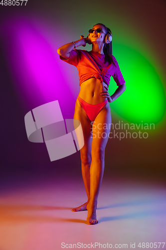 Image of Beautiful seductive girl in fashionable swimsuit on disco bicolored neon studio background in neon light. Summer, resort, fashion and weekend concept