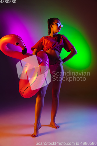 Image of Beautiful seductive girl in fashionable swimsuit on disco bicolored neon studio background in neon light. Summer, resort, fashion and weekend concept