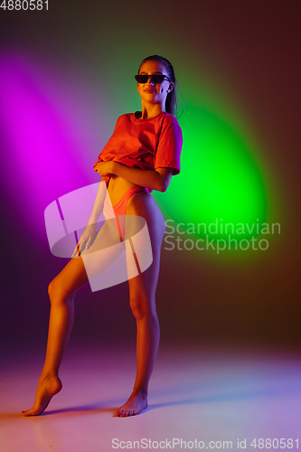 Image of Beautiful seductive girl in fashionable swimsuit on disco bicolored neon studio background in neon light. Summer, resort, fashion and weekend concept