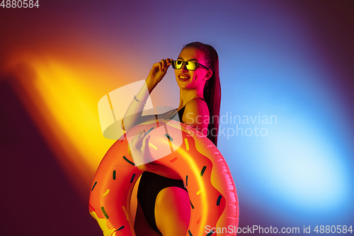 Image of Beautiful seductive girl in fashionable swimsuit on disco bicolored neon studio background in neon light. Summer, resort, fashion and weekend concept