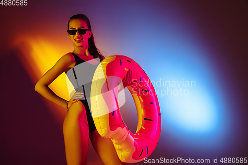 Image of Beautiful seductive girl in fashionable swimsuit on disco bicolored neon studio background in neon light. Summer, resort, fashion and weekend concept