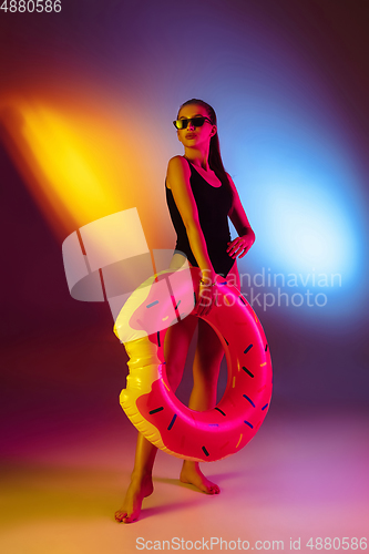 Image of Beautiful seductive girl in fashionable swimsuit on disco bicolored neon studio background in neon light. Summer, resort, fashion and weekend concept