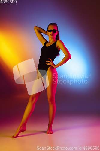 Image of Beautiful seductive girl in fashionable swimsuit on disco bicolored neon studio background in neon light. Summer, resort, fashion and weekend concept