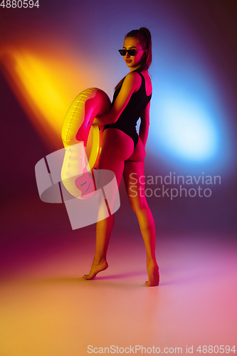 Image of Beautiful seductive girl in fashionable swimsuit on disco bicolored neon studio background in neon light. Summer, resort, fashion and weekend concept