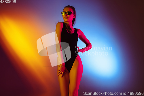 Image of Beautiful seductive girl in fashionable swimsuit on disco bicolored neon studio background in neon light. Summer, resort, fashion and weekend concept