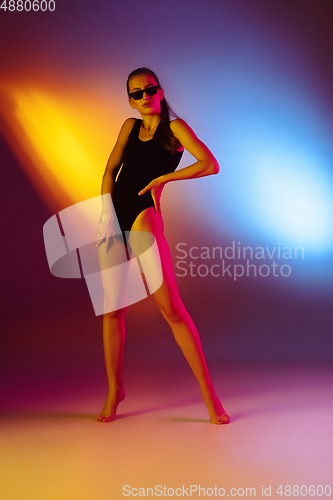 Image of Beautiful seductive girl in fashionable swimsuit on disco bicolored neon studio background in neon light. Summer, resort, fashion and weekend concept