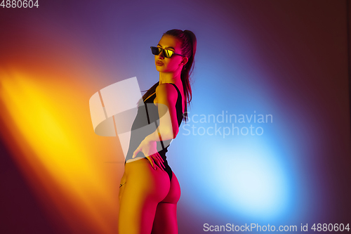Image of Beautiful seductive girl in fashionable swimsuit on disco bicolored neon studio background in neon light. Summer, resort, fashion and weekend concept