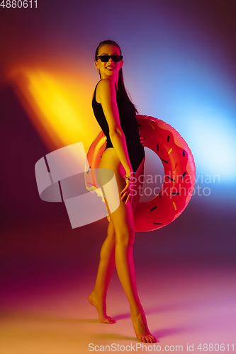 Image of Beautiful seductive girl in fashionable swimsuit on disco bicolored neon studio background in neon light. Summer, resort, fashion and weekend concept