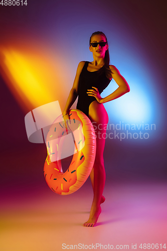 Image of Beautiful seductive girl in fashionable swimsuit on disco bicolored neon studio background in neon light. Summer, resort, fashion and weekend concept