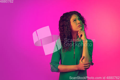 Image of African-american young woman\'s portrait isolated on gradient pink background in neon light