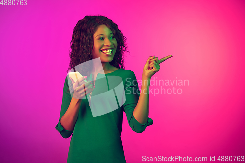 Image of African-american young woman\'s portrait isolated on gradient pink background in neon light