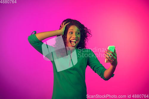 Image of African-american young woman\'s portrait isolated on gradient pink background in neon light