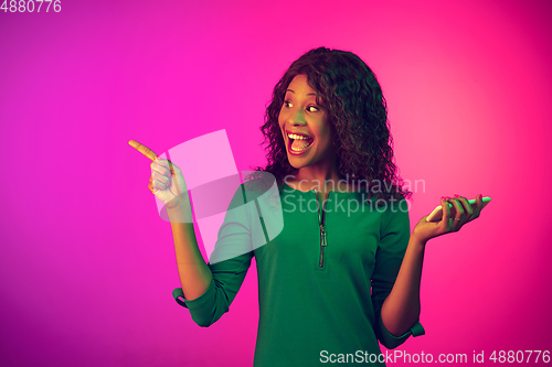 Image of African-american young woman\'s portrait isolated on gradient pink background in neon light