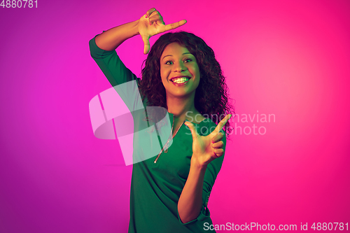 Image of African-american young woman\'s portrait isolated on gradient pink background in neon light