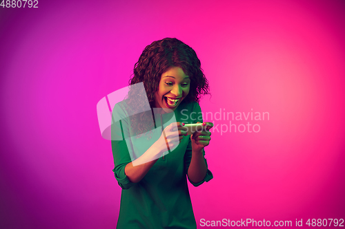 Image of African-american young woman\'s portrait isolated on gradient pink background in neon light