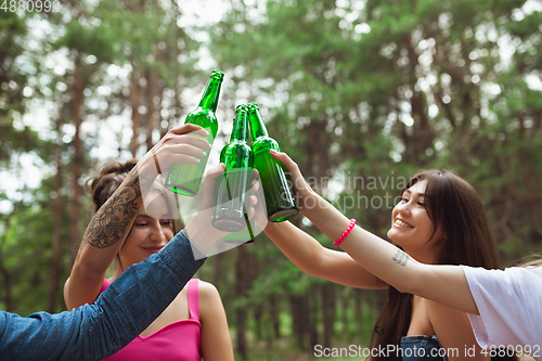 Image of Group of friends clinking beer bottles during picnic in summer forest. Lifestyle, friendship