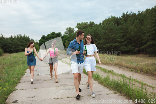 Image of Group of friends clinking beer bottles during picnic in summer forest. Lifestyle, friendship