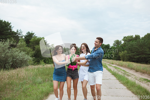 Image of Group of friends clinking beer bottles during picnic in summer forest. Lifestyle, friendship