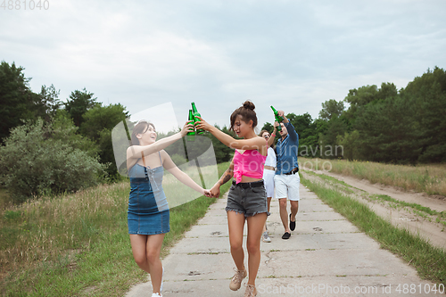 Image of Group of friends clinking beer bottles during picnic in summer forest. Lifestyle, friendship