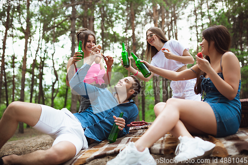 Image of Group of friends clinking beer bottles during picnic in summer forest. Lifestyle, friendship