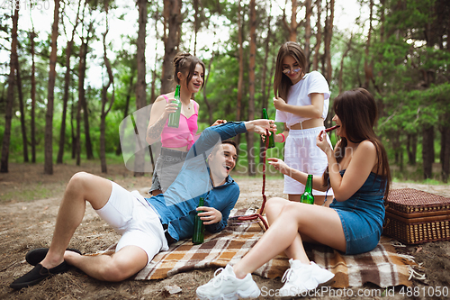 Image of Group of friends clinking beer bottles during picnic in summer forest. Lifestyle, friendship