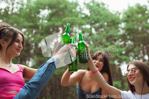 Image of Group of friends clinking beer bottles during picnic in summer forest. Lifestyle, friendship