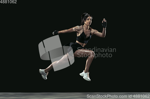 Image of Beautiful young female athlete practicing on black studio background, full length portrait