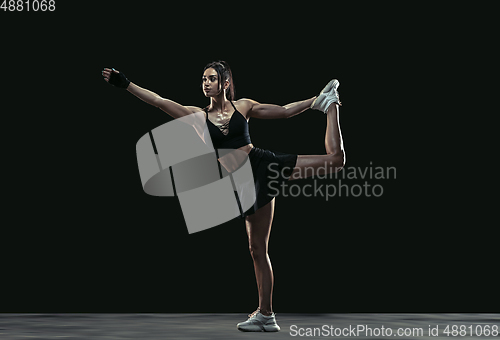 Image of Beautiful young female athlete practicing on black studio background, full length portrait