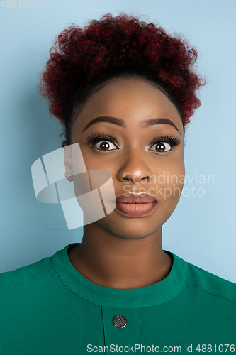 Image of African-american beautiful young woman\'s close up portrait on blue studio background, emotional and expressive. Copyspace for ad.