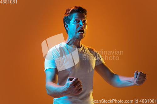 Image of Caucasian beautiful young man\'s portrait on gradient orange studio background, emotional and expressive. Copyspace for ad.