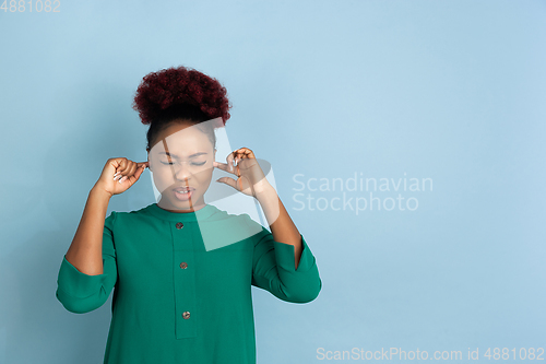 Image of African-american beautiful young woman\'s portrait on blue studio background, emotional and expressive. Copyspace for ad.