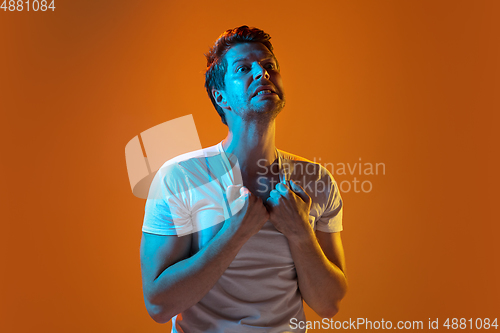 Image of Caucasian beautiful young man\'s portrait on gradient orange studio background, emotional and expressive. Copyspace for ad.