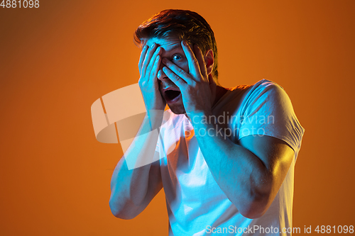 Image of Caucasian beautiful young man\'s portrait on gradient orange studio background, emotional and expressive. Copyspace for ad.