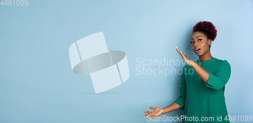 Image of African-american beautiful young woman\'s portrait on blue studio background, emotional and expressive. Copyspace for ad.