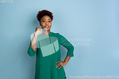 Image of African-american beautiful young woman\'s portrait on blue studio background, emotional and expressive. Copyspace for ad.