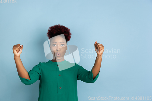 Image of African-american beautiful young woman\'s portrait on blue studio background, emotional and expressive. Copyspace for ad.