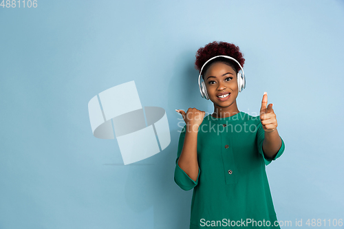 Image of African-american beautiful young woman\'s portrait on blue studio background, emotional and expressive. Copyspace for ad.