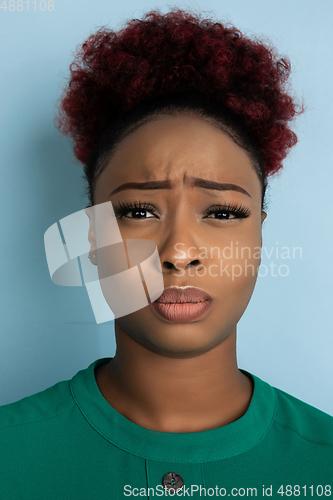 Image of African-american beautiful young woman\'s close up portrait on blue studio background, emotional and expressive. Copyspace for ad.