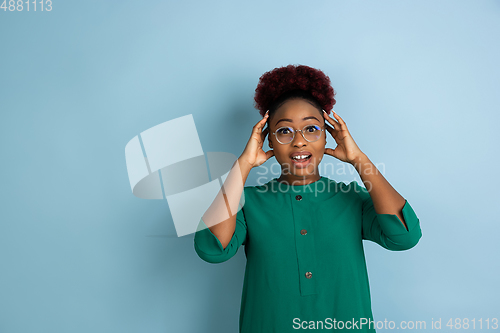 Image of African-american beautiful young woman\'s portrait on blue studio background, emotional and expressive. Copyspace for ad.