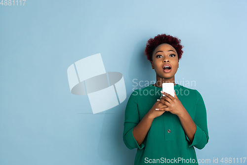 Image of African-american beautiful young woman\'s portrait on blue studio background, emotional and expressive. Copyspace for ad.