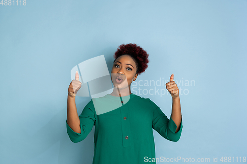 Image of African-american beautiful young woman\'s portrait on blue studio background, emotional and expressive. Copyspace for ad.
