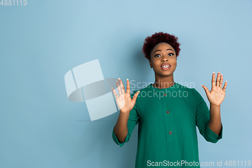 Image of African-american beautiful young woman\'s portrait on blue studio background, emotional and expressive. Copyspace for ad.