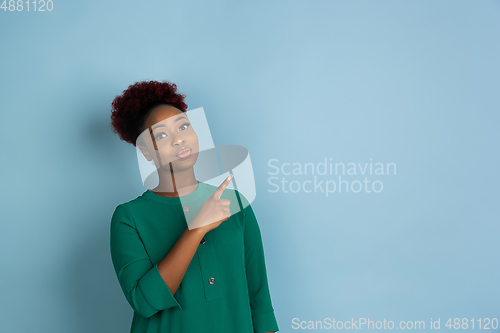 Image of African-american beautiful young woman\'s portrait on blue studio background, emotional and expressive. Copyspace for ad.