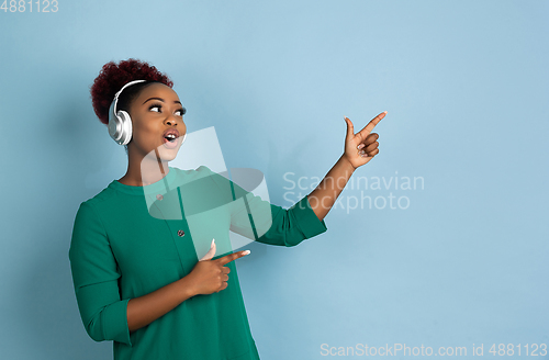 Image of African-american beautiful young woman\'s portrait on blue studio background, emotional and expressive. Copyspace for ad.