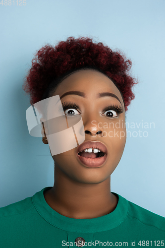 Image of African-american beautiful young woman\'s close up portrait on blue studio background, emotional and expressive. Copyspace for ad.