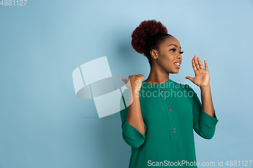 Image of African-american beautiful young woman\'s portrait on blue studio background, emotional and expressive. Copyspace for ad.