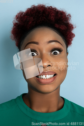 Image of African-american beautiful young woman\'s close up portrait on blue studio background, emotional and expressive. Copyspace for ad.