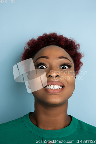 Image of African-american beautiful young woman\'s close up portrait on blue studio background, emotional and expressive. Copyspace for ad.