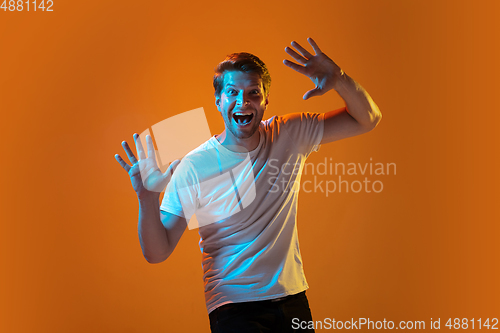 Image of Caucasian beautiful young man\'s portrait on gradient orange studio background, emotional and expressive. Copyspace for ad.